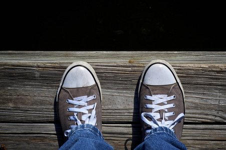 低头看脚低头看着穿着鞋的运动鞋在码头的边缘,水是黑暗的,就像看着