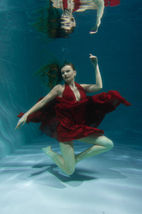 一个美丽的自由潜水员，一个人穿着红色的长裙，独自在深水中游泳