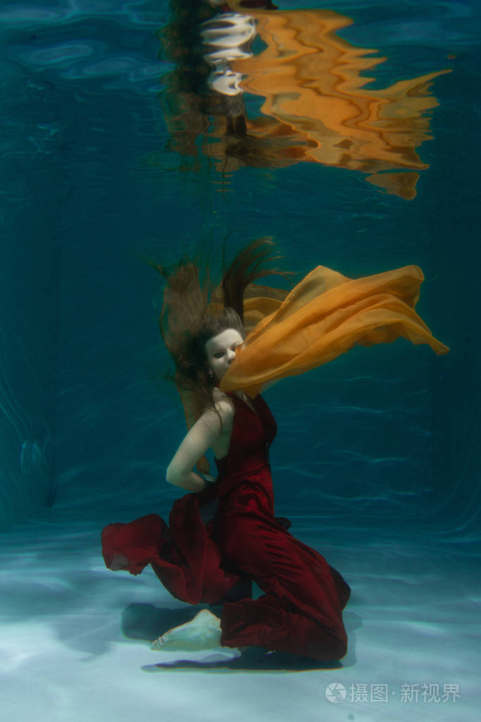 美丽的自由的自由潜水员一个人穿着红色的长裙独自在深水中游泳