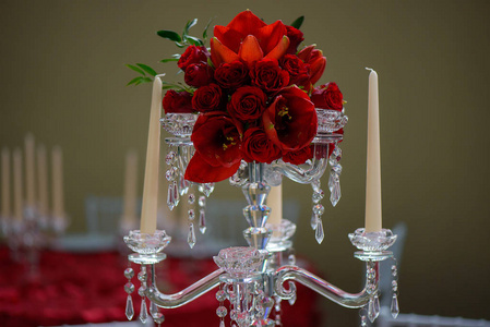 一个浪漫的正式桌子中心，一个美丽的水晶烛台风格的烛台，有八个扇贝，作为烛台和红色郁金香和玫瑰花束