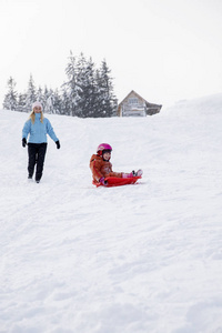 妈妈和女儿骑在雪橇上从雪地上。骑雪橇从雪山上骑下来。雪橇, 冬季乐趣, 雪, 家庭雪橇骑行