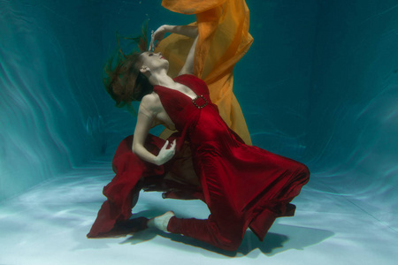 一个美丽的自由潜水员，一个人穿着红色的长裙，独自在深水中游泳