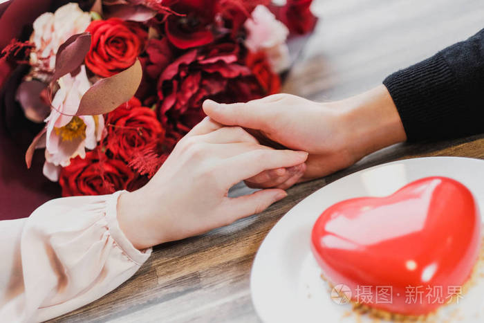 女人和男人紧紧地握着手在咖啡馆桌子的背景上背景上的心形的花束和