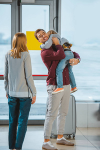幸福的父亲抱着女儿在机场的妻子身边