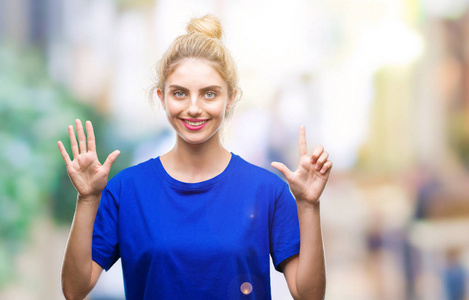 年轻漂亮的金发碧眼的女人穿着蓝色的t恤，在孤立的背景上，用手指举着七号，微笑着自信和快乐。