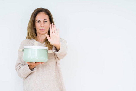 中年家庭主妇女人拿着铁锅在孤立的背景上张开手做停止标志，严肃自信地表达防御手势