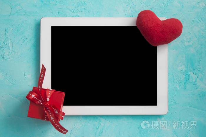 白色的平板电脑在蓝色的表面与浪漫的礼物和毛绒的心。 快乐情人节卡片。