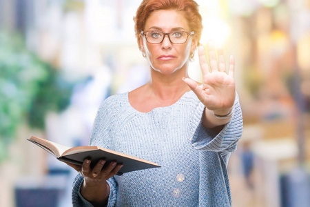 高白种人妇女在孤立的背景下阅读一本书，张开手做停止标志，严肃而自信地表达防御手势