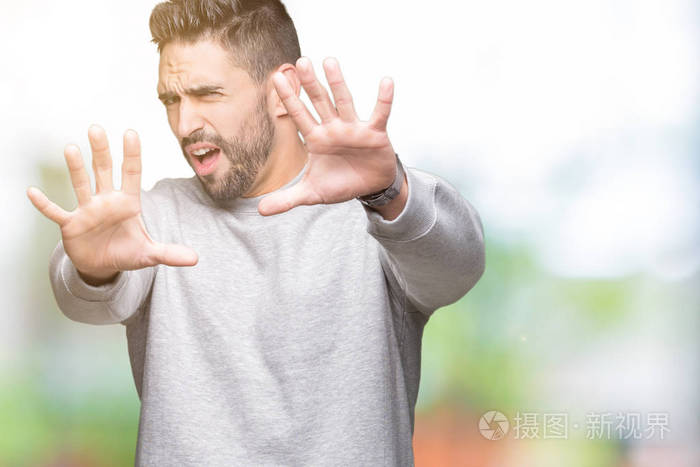 年轻的英俊男子穿着运动衫在孤立的背景上害怕和恐惧的表情停止手势