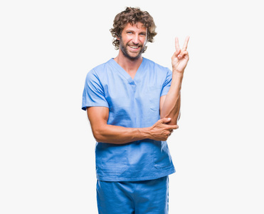 英俊的西班牙裔外科医生，男人在孤立的背景上微笑，快乐的脸对着镜头眨眼，做胜利的标志。 二号。