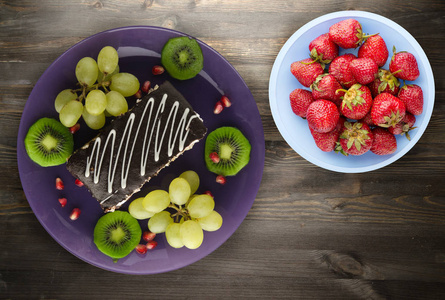 蛋糕和水果的甜点葡萄猕猴桃在木制背景上。 餐盘上的甜点