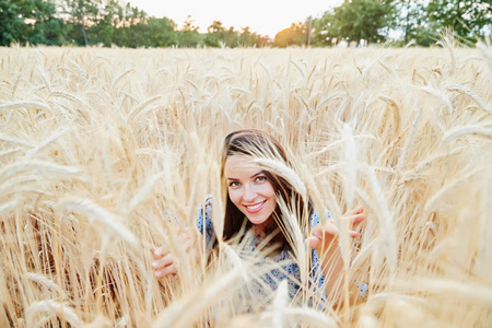 这位美丽的年轻姑娘长着深色头发，在田野里摆姿势，麦色日落，灯光，微笑，调情，快乐的蓝色连衣裙，法国普罗旺斯