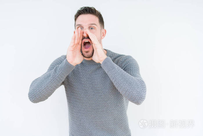 年轻的帅哥穿着休闲毛衣,在孤立的背景下大声喊叫,双手捂住嘴