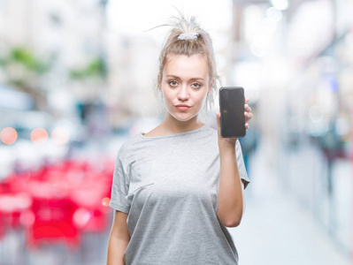 年轻的金发女人在孤立的背景上显示智能手机屏幕，聪明的脸上有自信的表情，严肃的思考