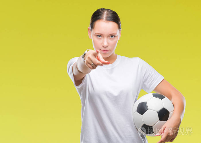 年轻美丽的白种人女子手中拿着足球球在孤立的背景上，手指指向相机，向你手势正面和自信的手势