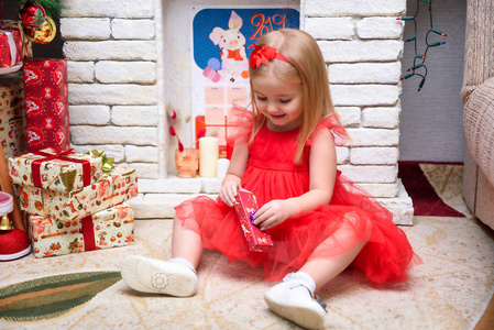 概念肖像一个可爱的美丽女孩在新年与礼物背景的圣诞树，穿着时尚的红色连衣裙。 她坐着有不同的情绪。