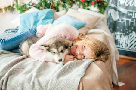 可爱的女孩，一头金发，在家里和一只可爱的小狗玩耍，房间里装饰着圣诞节