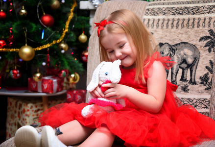 概念肖像一个可爱的美丽女孩在新年与礼物背景的圣诞树，穿着时尚的红色连衣裙。 她坐着有不同的情绪。图片