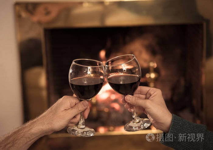 亲密的浪漫夫妇举着两个红酒杯在火中品尝在寒假假期圣诞节或周年纪念