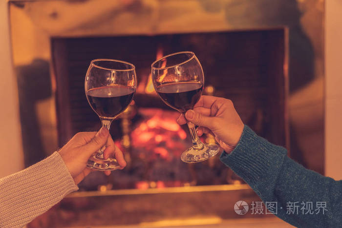 亲密的浪漫夫妇举着两个红酒杯在火中品尝在寒假假期圣诞节或周年纪念