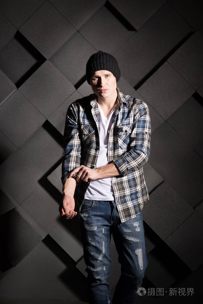 穿着格子衬衫和黑色帽子,摆着黑色结构背景的年轻潮人