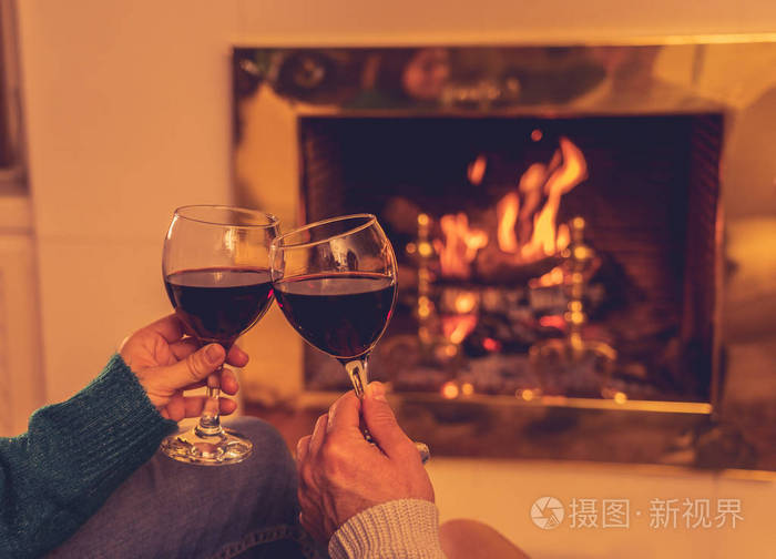 亲密的浪漫夫妇举着两个红酒杯在火中品尝,在寒假假期圣诞节或周年