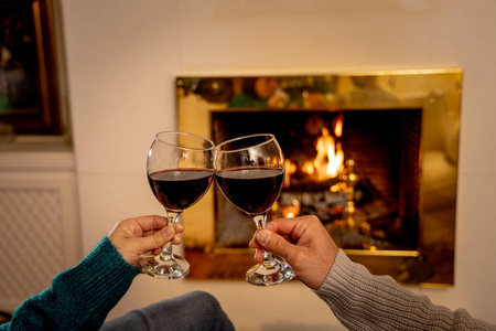 亲密的浪漫夫妇举着两个红酒杯在火中品尝，在寒假假期圣诞节或周年纪念的概念中，一起在小屋的壁炉旁庆祝快乐的时刻。