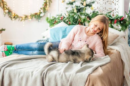 可爱的女孩，一头金发，在家里和一只可爱的小狗玩耍，房间里装饰着圣诞节
