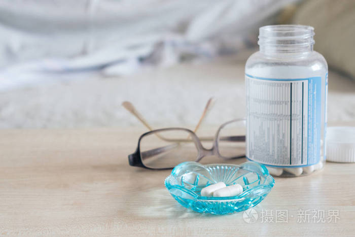 安眠药催眠药物镇静褪黑素玻璃杯中的胶囊玻璃杯和一瓶药片放在床旁的