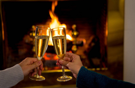 拿着两个香槟杯,在敞开的木头壁炉边品尝,在寒假和情人节或周年纪念日