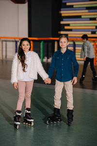 两个微笑着的漂亮孩子手牵着手站在溜冰旁