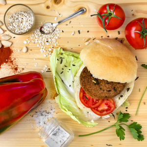 纯素汉堡与新鲜蔬菜在木制桌子顶部视图。 健康快餐形象主题。