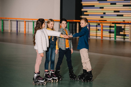 穿滑轮滑冰鞋的微笑的孩子们呆在溜冰场上，一起伸展双手