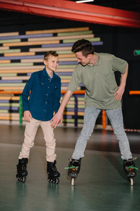 英俊的年轻教练给微笑的男孩做滑冰指导
