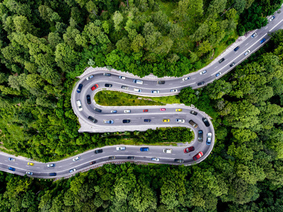 蜿蜒的道路充满了交通。 绿林中的高峰时间交通。 生态概念。 综合照片