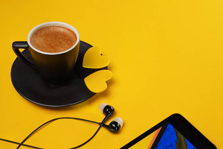 这杯咖啡和带耳机的智能手机躺在黄色的背景上