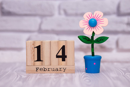 2月14日,每月14日在木制日历上,白色砖块背景上有玩具花. 情人节快乐.