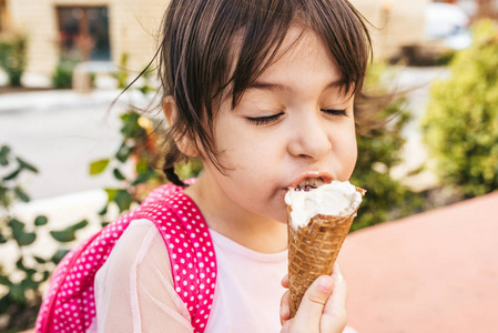 品尝的甜点特写形象可爱的小女孩坐在城市街道上,在户外吃冰淇淋.