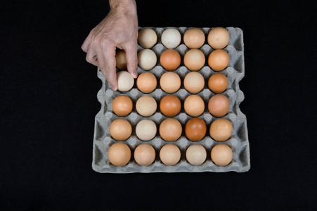 雄性手从纸板蛋盒中取出一个鸡蛋，放在黑色毛毡背景上。