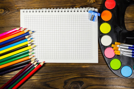 木制背景上的一套绘图工具。 空白笔记本水彩颜料画笔彩色铅笔书桌