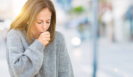 美丽的中年妇女穿着冬季毛衣，在孤立的背景下感到不适和咳嗽，作为感冒或支气管炎的症状。 医疗保健概念。