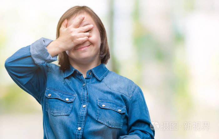 年轻的成年妇女患有唐氏综合症,在孤立的背景上微笑和笑,用手捂着眼睛