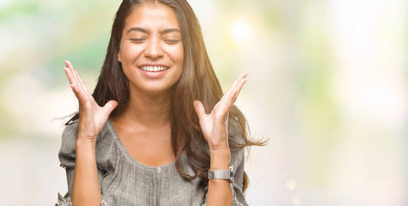 年轻美丽的阿拉伯女人在孤立的背景上庆祝疯狂和疯狂的成功，举起手臂和闭上眼睛尖叫兴奋。 赢家概念