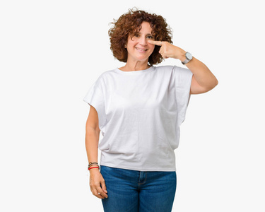年轻的中老年妇女穿着白色T恤，背景偏僻，用手指着脸鼻子微笑，开朗