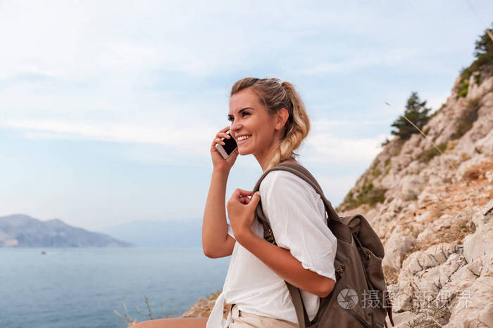 徒步旅行者年轻的女人带着背包，用智能手机在徒步旅行中寻找风景