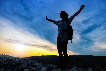 日落时分，徒步旅行者女性的轮廓在山顶上抬起手臂