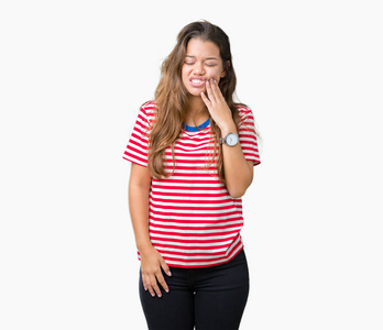 年轻漂亮的黑发女人，穿着条纹T恤，在孤立的背景上，用手触摸嘴，因为牙痛或牙齿上的牙齿疾病，表情痛苦。 牙医的概念。