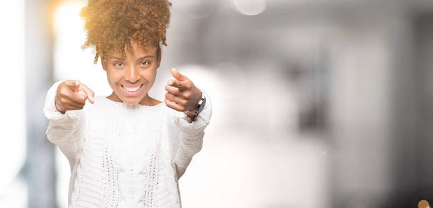 美丽的年轻的非洲裔美国妇女穿着冬季毛衣，背景偏僻，指着你和相机，手指微笑，积极和快乐
