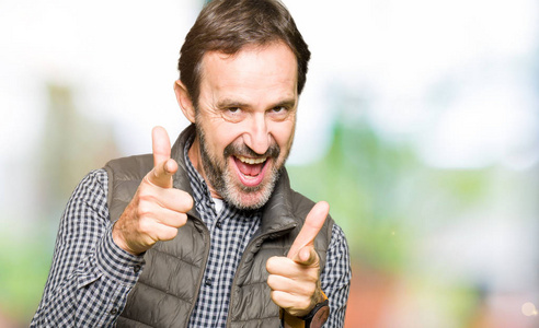 英俊的男人穿着冬天的背心,手指着相机,脸上洋溢着快乐和有趣的表情