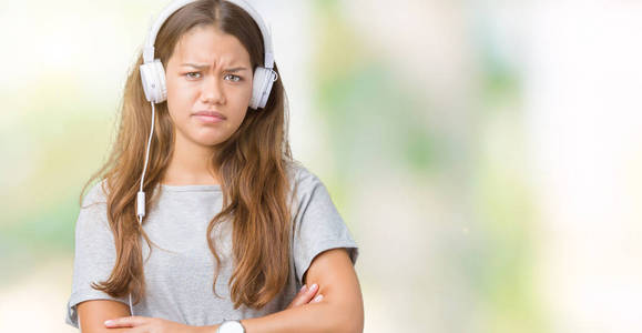 年轻漂亮的女人戴着耳机听音乐，在孤立的背景怀疑和紧张的不赞成的表情上，交叉的手臂。 消极的人。